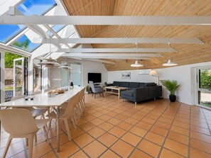 Ein geräumiger Wohnbereich mit hoher Decke, einem Esstisch mit Stühlen, einer Couch und einem Fernseher.