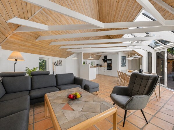 Ein großzügiger Wohnbereich mit modernem Design, ausgestattet mit einem großen Sofa, einem Couchtisch mit Obst und einem Essbereich mit Stühlen.