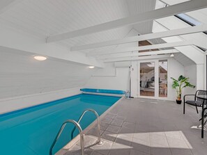 Une piscine intérieure à l’eau d’un bleu limpide, avec un sol carrelé et un plafond blanc agrémenté de lucarnes.