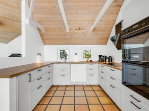 Eine moderne Küche mit weißen Schränken, einer Holzbalkendecke und einem Fliesenboden.