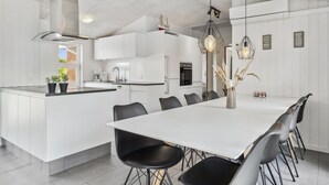 A modern kitchen with white cabinetry, a central island, and a dining area with a long table and chairs. - "Jonke" - 800m from the sea by Interhome (Blåvand)