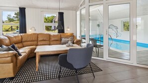 A modern living room with a leather sofa, a dining table, and a chair. There is a large window with a view of a swimming pool and a dolphin mural. - "Jonke" - 800m from the sea by Interhome (Blåvand)