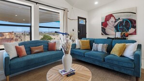 A living room with a blue sofa, a round coffee table, and a painting on the wall. - Summer Relax & Unwind @ Genesis Oasis - Wifi + Spa! Pet Friendly! (Joshua Tree)