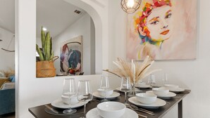 A dining table set with white plates, bowls, and glasses, a vase with dried plants, and a painting on the wall. - Summer Relax & Unwind @ Genesis Oasis - Wifi + Spa! Pet Friendly! (Joshua Tree)