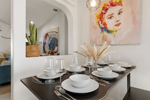 A dining table set with white plates, bowls, and glasses, a vase with dried plants, and a painting on the wall. - Summer Relax & Unwind @ Genesis Oasis - Wifi + Spa! Pet Friendly! (Joshua Tree)