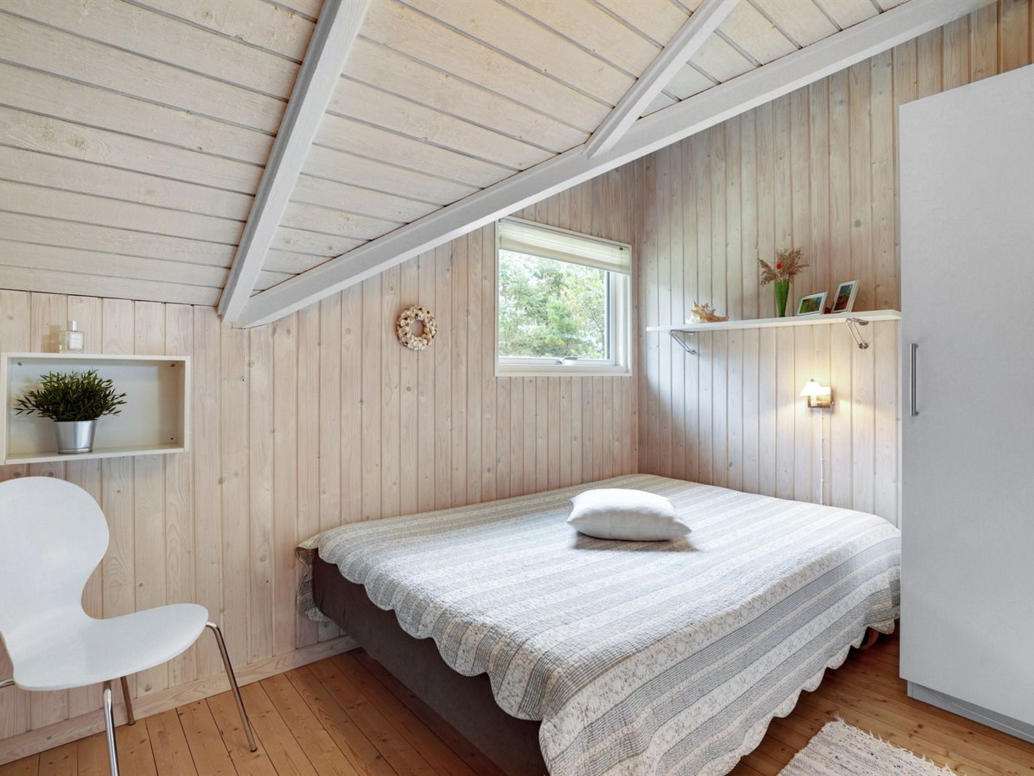 Une chambre à coucher avec un lit, une chaise, une fenêtre, des étagères décorées et un plafond en bois.