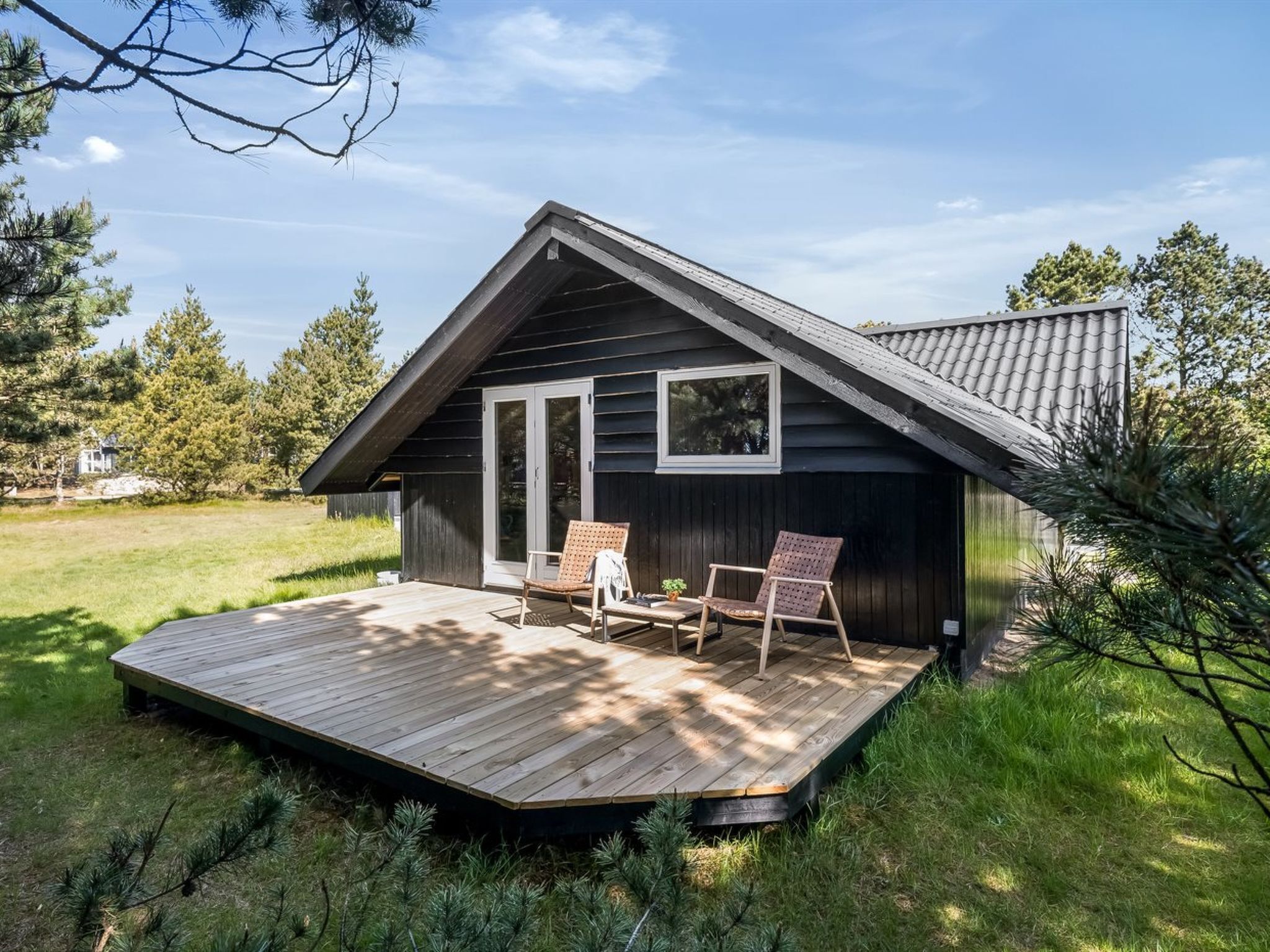 A cabin with a wooden deck, two chairs, and a table.