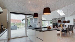 Une cuisine moderne dotée d’un îlot central, de grandes fenêtres et d’un coin repas avec des chaises.