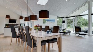 Un espace de salle à manger moderne, doté d’une grande table, de chaises et de luminaires suspendus.