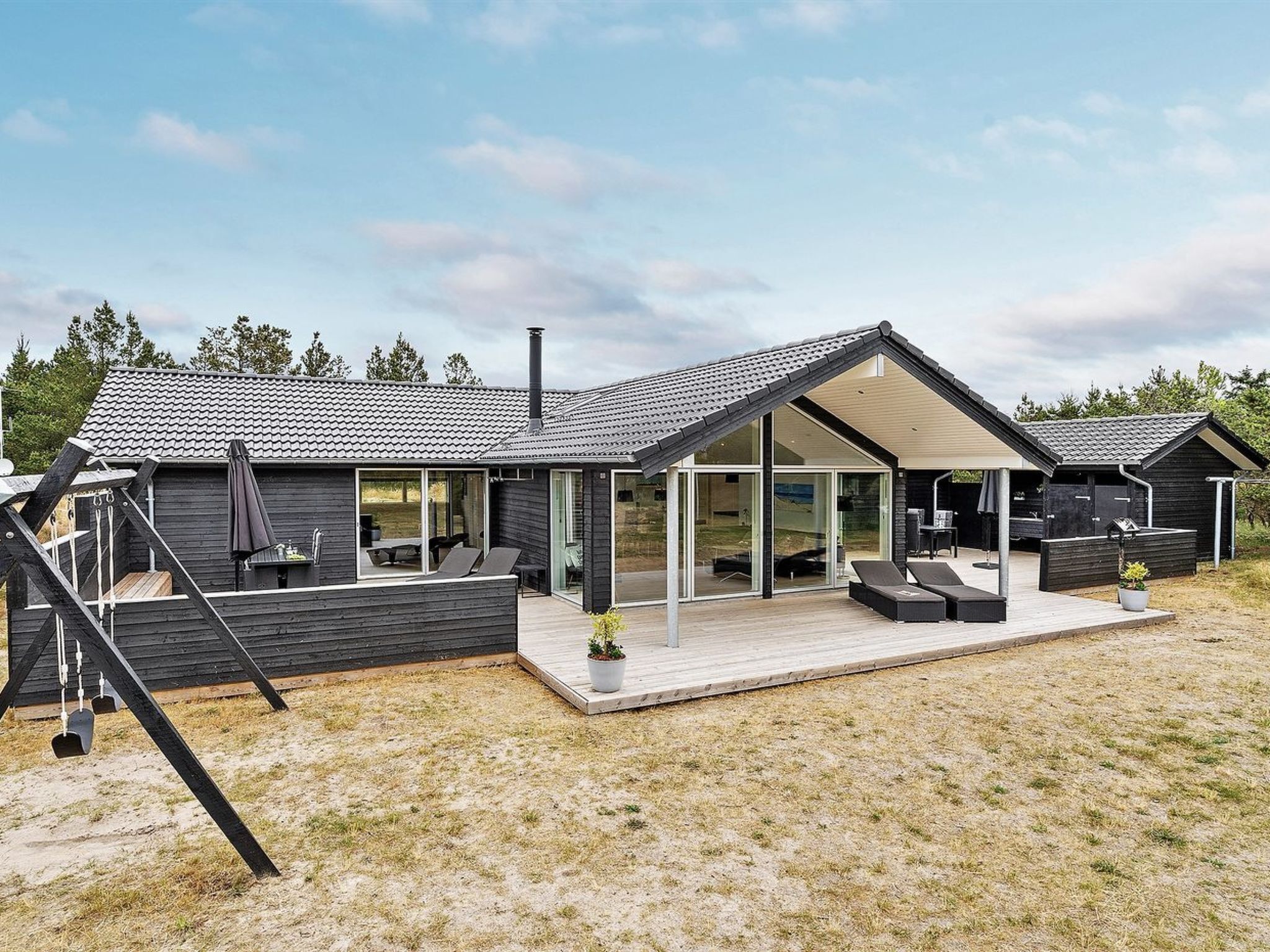 Une maison moderne dotée d’une grande terrasse, d’un espace salon extérieur et d’un patio couvert.