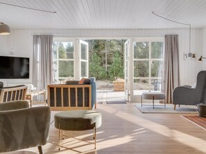 Een ruime woonkamer met een grote televisie, comfortabele zithoek en uitzicht door grote ramen.