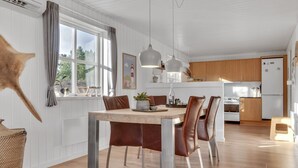 A modern kitchen with wooden cabinets, a dining table with chairs, pendant lights, and a star decoration on the wall. - "Harpa" - 2.5km from the sea by Interhome (Blåvand)