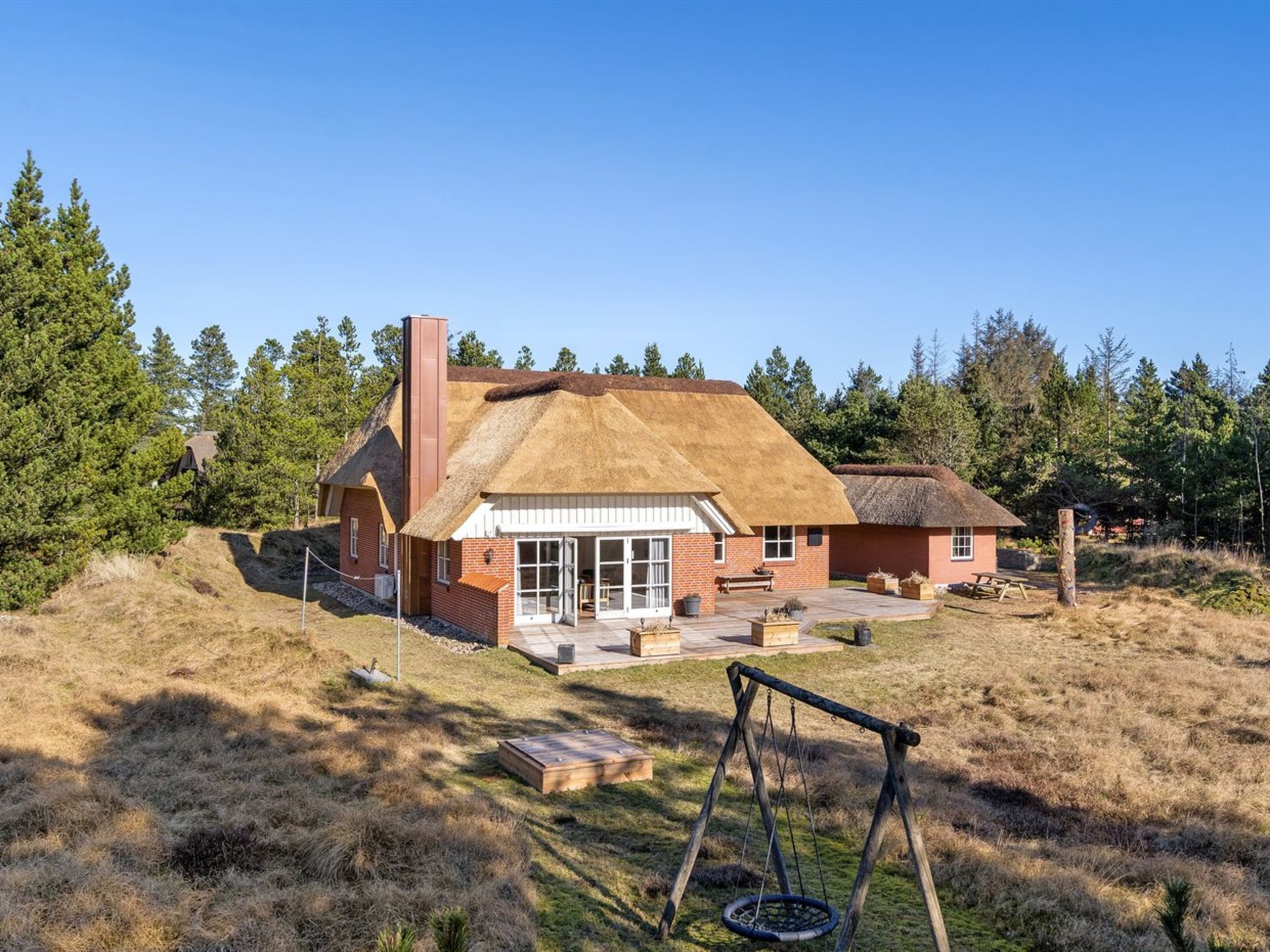 A rustic house with a thatched roof, a chimney, and a patio area with a swing set.