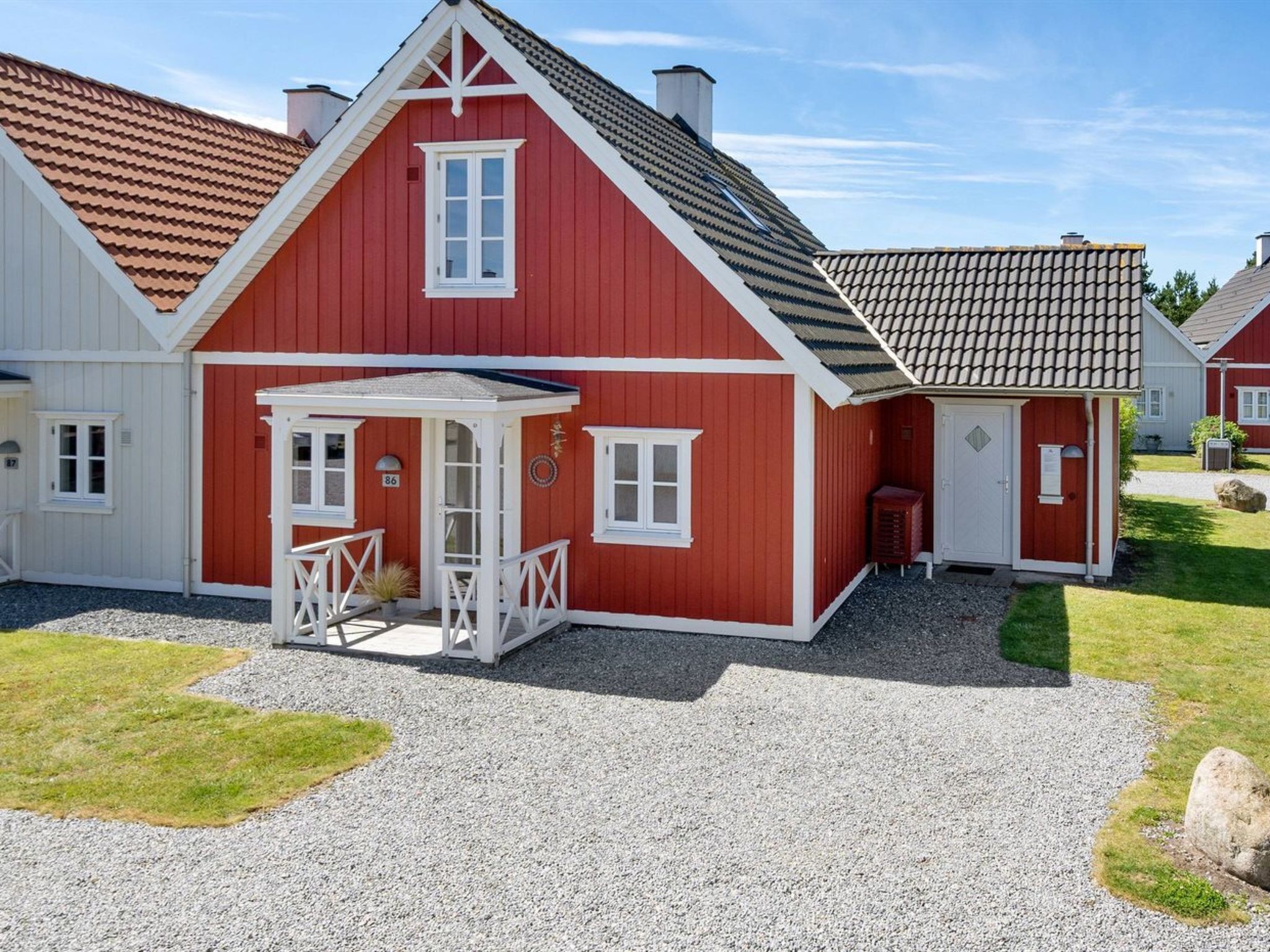 A red and white house with a porch, a small garden, and a gravel driveway.