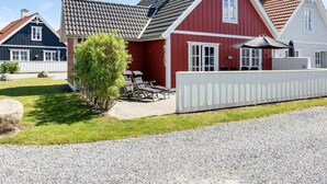 A red house with a grey roof, a white fence, and a small garden with a tree and two lounge chairs. - "Todorka" - 800m from the sea by Interhome (Blåvand)