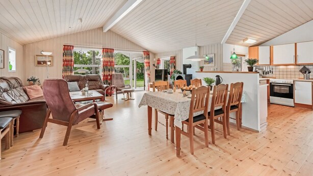 Un grand espace de vie comprenant un coin repas avec une table, des canapés et une cuisine équipée de meubles en bois et d’une cuisinière.