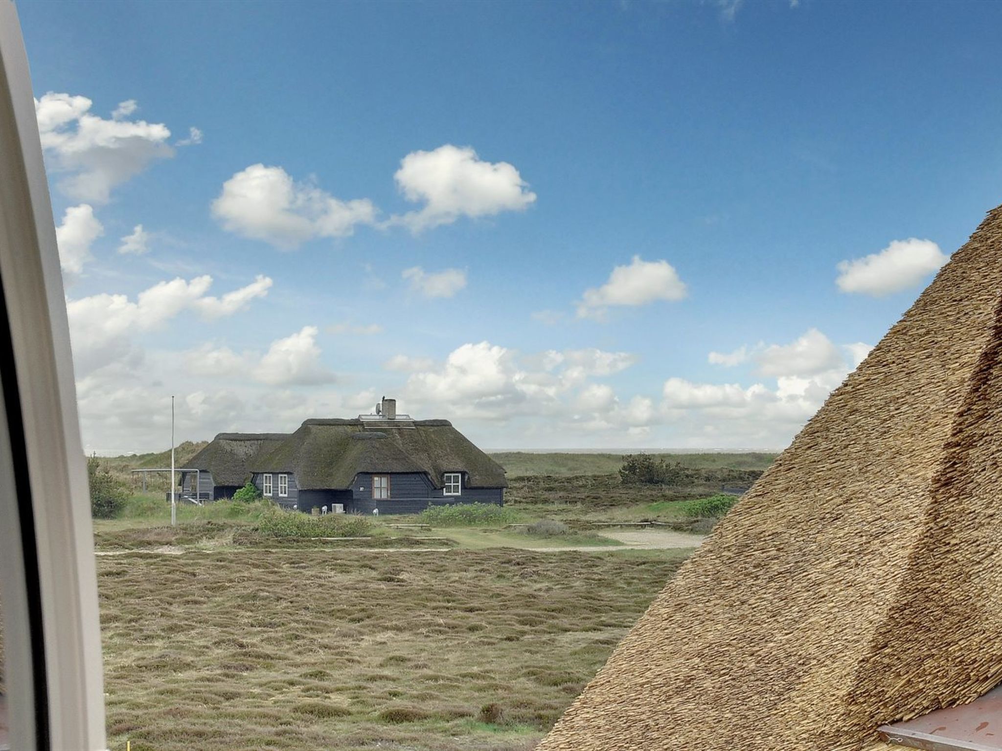 A traditional house with a thatched roof, surrounded by a grassy landscape.