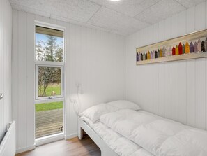 A bedroom with a single bed, a window with a view of a green landscape, and a colorful painting on the wall.