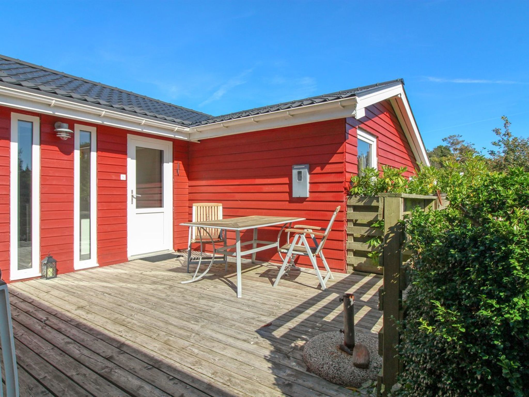 Een rood gebouw met een houten terras, een tafel en stoelen.