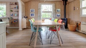 A cozy dining area with a wooden table and colorful chairs, a bookshelf, and a fireplace.