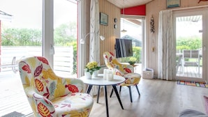 A cozy room with a wooden ceiling, large windows, a round table with chairs, and a sail wheel decoration.