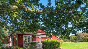 A red house with a deck, surrounded by greenery and a well-maintained lawn.