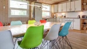 A modern kitchen with wooden cabinets, a large island with colorful chairs, and a window providing natural light.