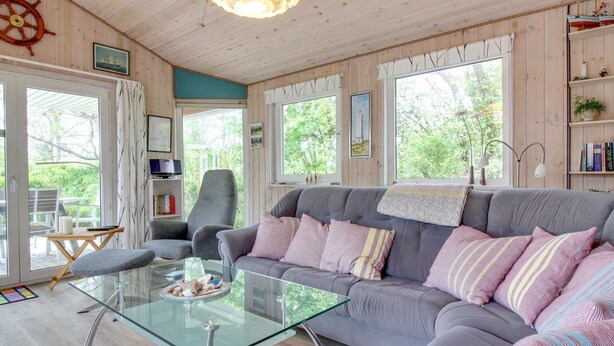 A cozy living room with a grey sofa, glass coffee table, and wooden walls.