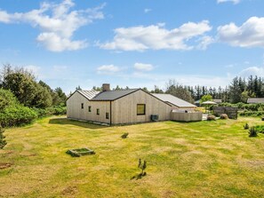 A modern wooden house with a metal roof, surrounded by a well-maintained lawn and dense forest.
