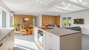 A modern kitchen with a central island, wooden accents, and a dining area with a table and chairs. - "Gunny" - 500m to the fjord by Interhome (Blåvand)