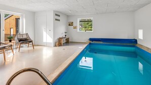 A modern indoor swimming pool with a clear view of the sky through a window, a wooden bench, and a wicker chair. - "Gunny" - 500m to the fjord by Interhome (Blåvand)
