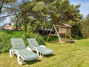Relax in a serene outdoor setting with a playhouse, lounge chairs, and lush greenery.