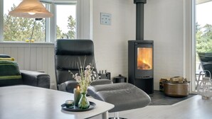 Una sala de estar moderna con un sofá de cuero negro, un florero de vidrio con flores, una mesa con una vela y un estufa de leña.