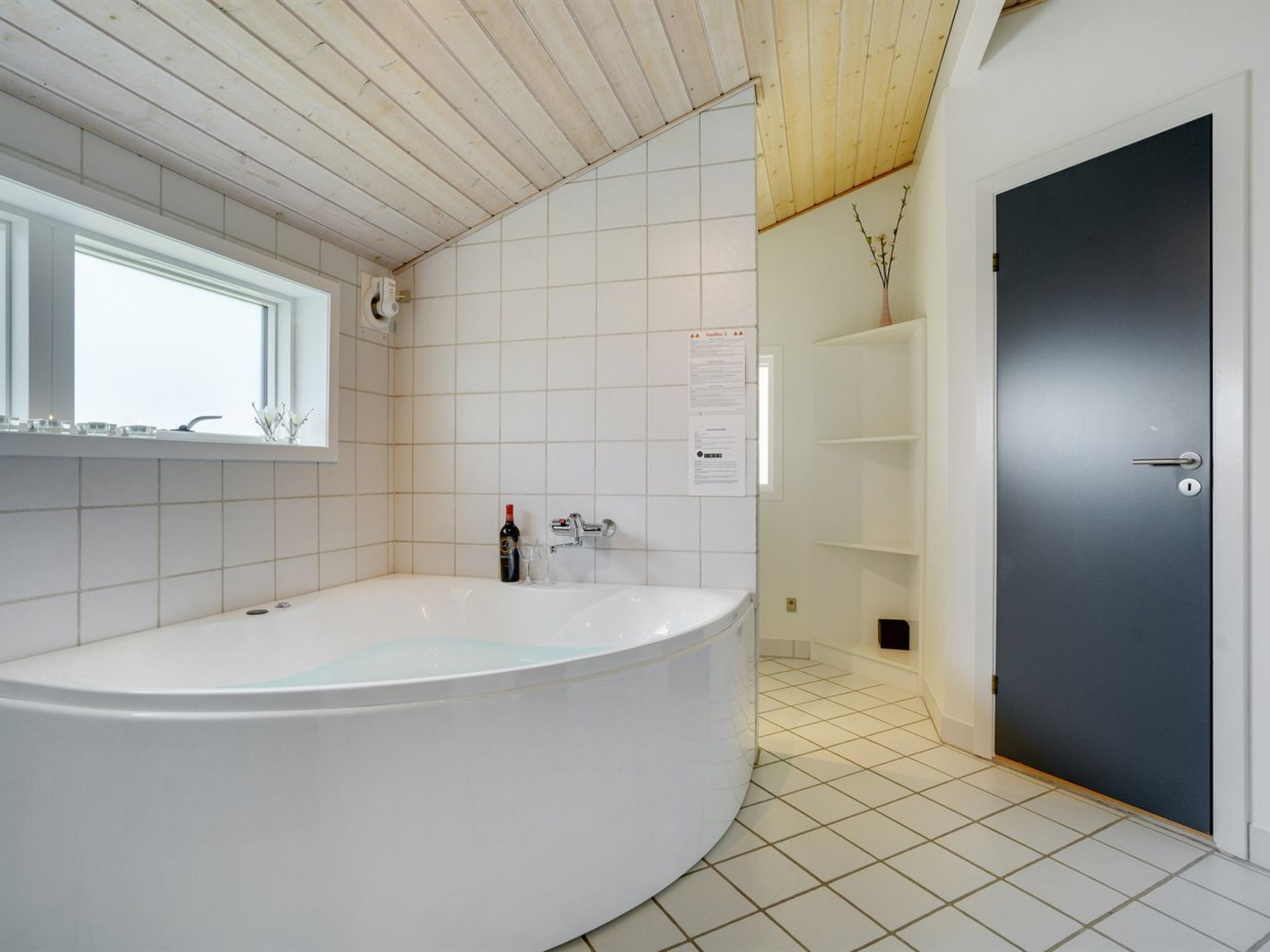 Une salle de bain moderne avec une baignoire sur pieds, une fenêtre et une porte sombre.