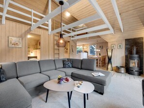 Un salon moderne avec un canapé d’angle, deux petites tables rondes et une cheminée.