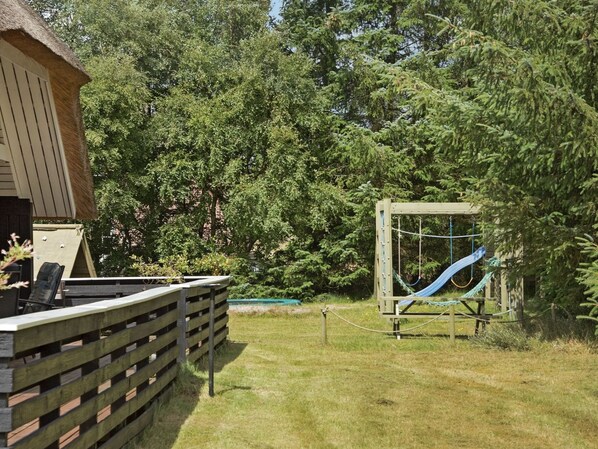Een houten terras met een hangmat en schommel in een gazon met bomen.