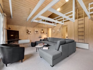 Een moderne woonkamer met een hoekbank, een zwarte fauteuil, een flatscreen-tv en een open haard.