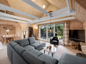 Een moderne woonkamer met een hoekbank, een flatscreen televisie en een eethoek met tafel en stoelen.