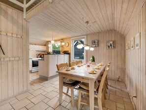 Een houten interieur met een eethoek, keuken en uitzicht door een raam.