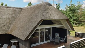 A modern house with a thatched roof, a deck with outdoor furniture, and a large glass door leading to an interior space. - "Patrik" - 1.4km from the sea by Interhome (Blåvand)