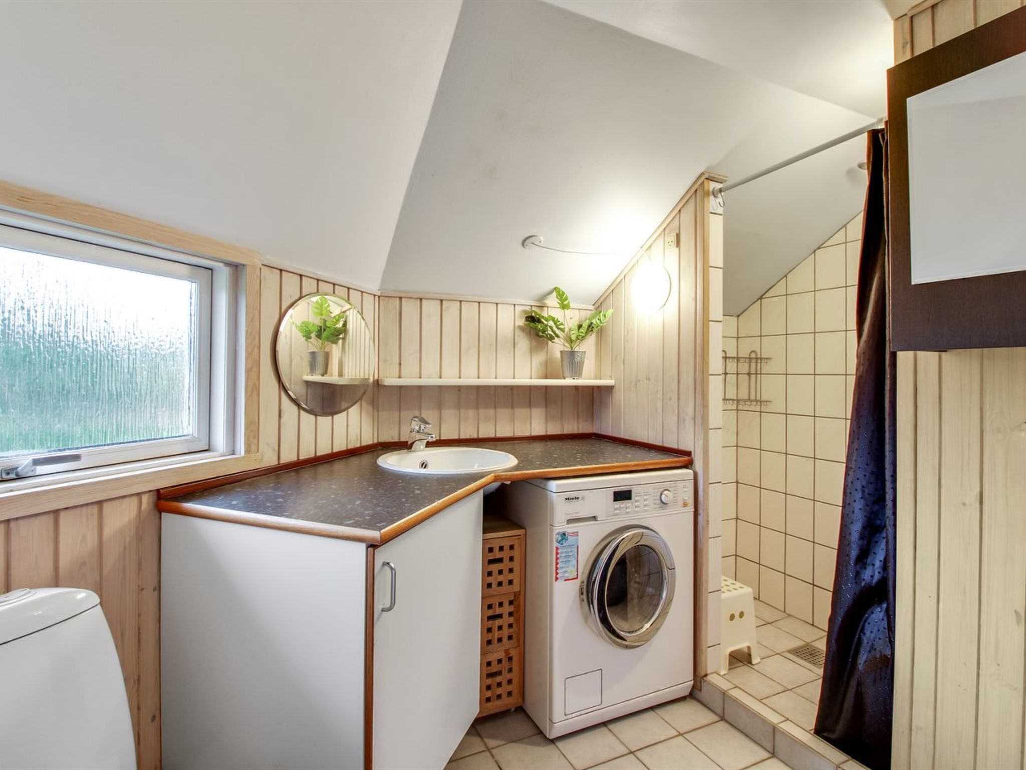 A compact bathroom with a sink, mirror, washing machine, and a shower area.