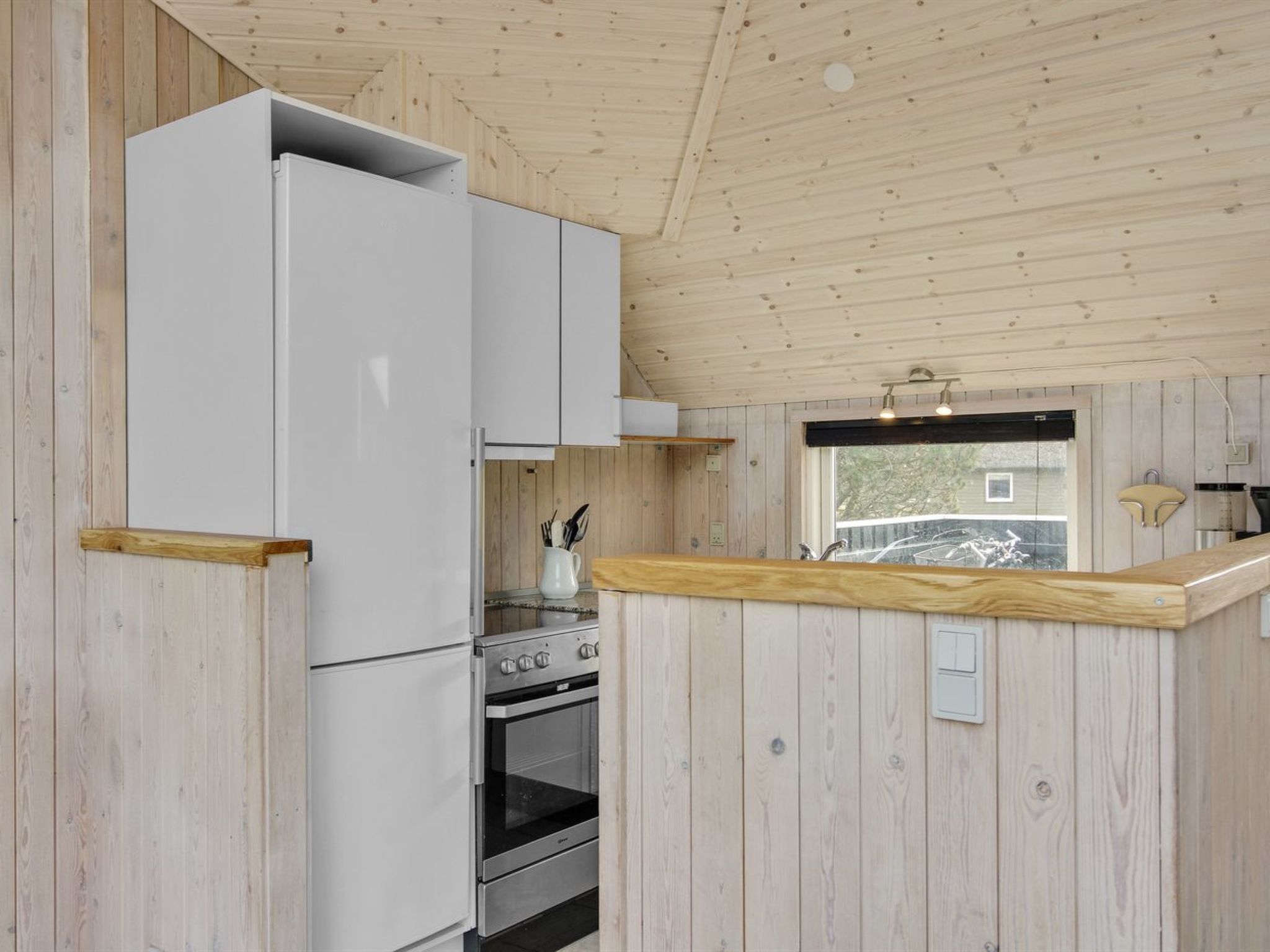 A compact kitchen with wooden walls, a white refrigerator, a stove, and a sink.