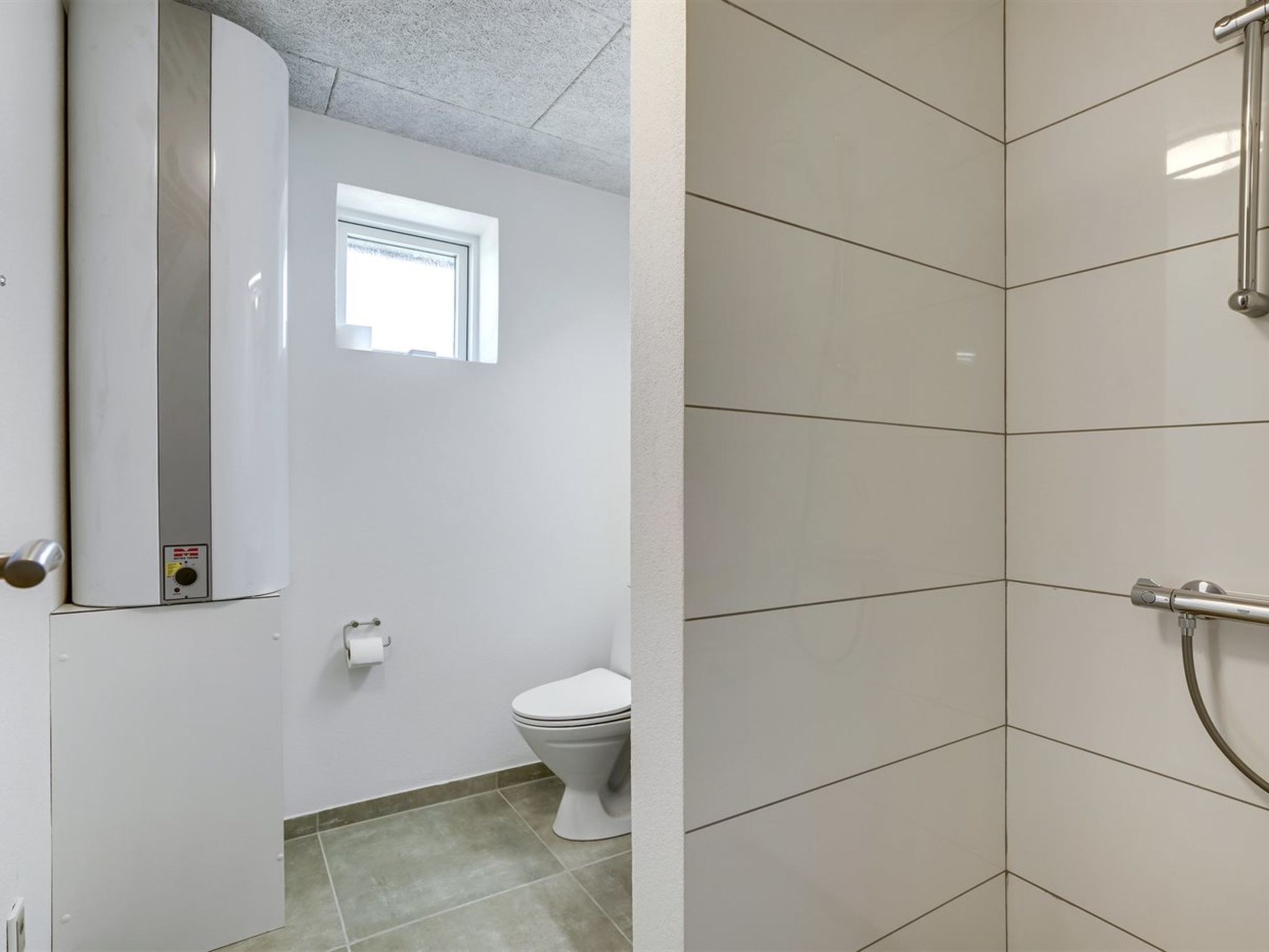 A bathroom with a toilet, a window, and a shower area.