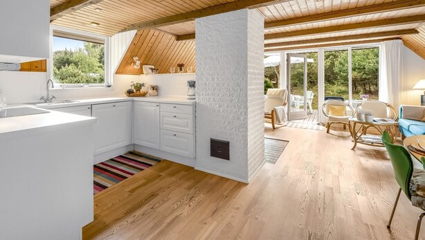 A modern kitchen with white cabinets, a wooden ceiling, and a view of greenery outside.