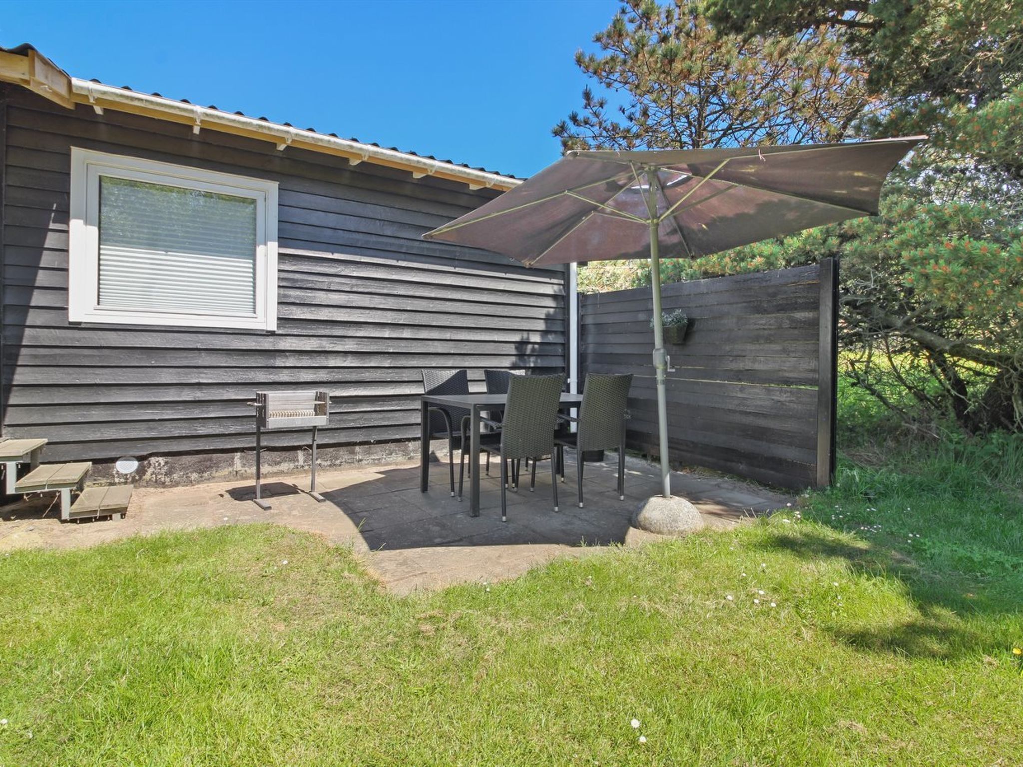 Un espace extérieur aménagé avec une table et des chaises, un barbecue et un grand parasol.