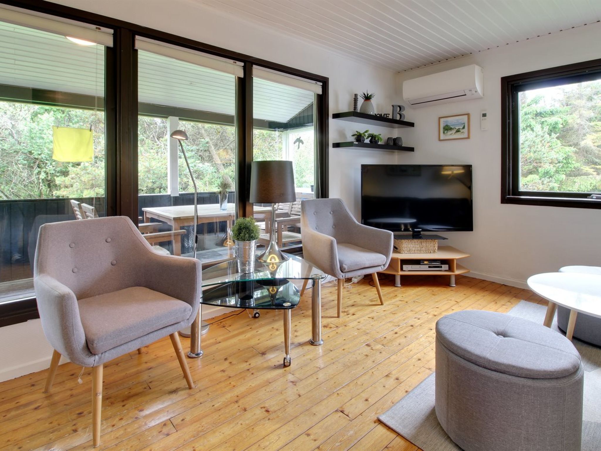 A modern living room with a large TV, comfortable seating, and large windows offering a view of the outdoors.