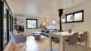 Una sala de estar moderna con piso de madera, un comedor con mesa y sillas, un sofá y un ventanal que proporciona luz natural.