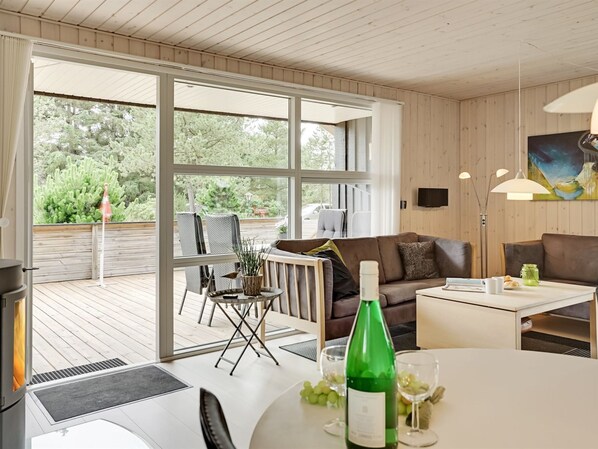 A modern living room with a large sliding glass door leading to an outdoor deck, a brown leather sofa, a white coffee table, and a bottle of wine.