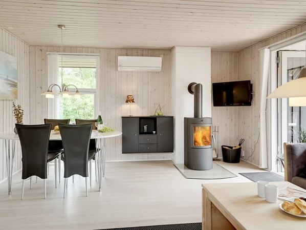 A modern kitchen with a wood stove, a dining area with chairs and a table, and a TV mounted on the wall.
