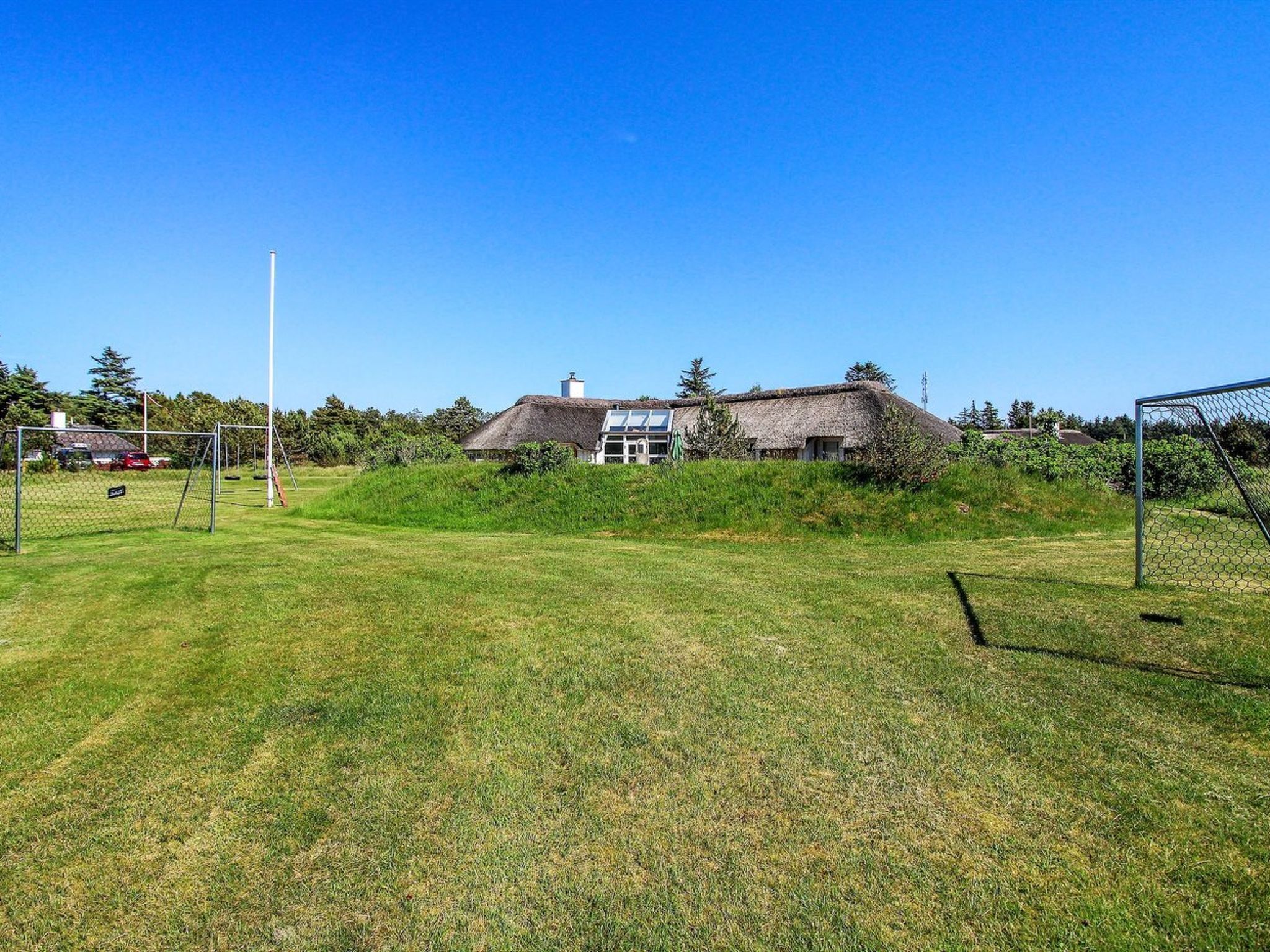 A thatched-roof house with a visible chimney, surrounded by a grassy field and a soccer goal.